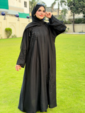 Woman wearing a black abaya with floral embroidery on a grassy field