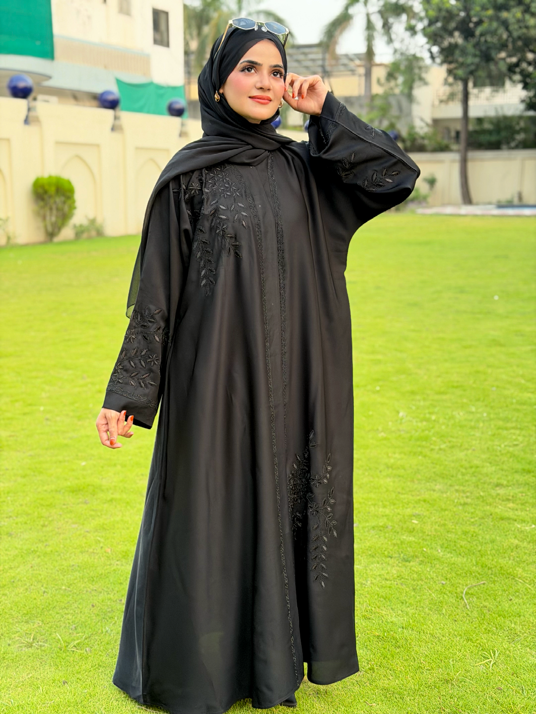 Woman wearing a black abaya with floral embroidery on a grassy field