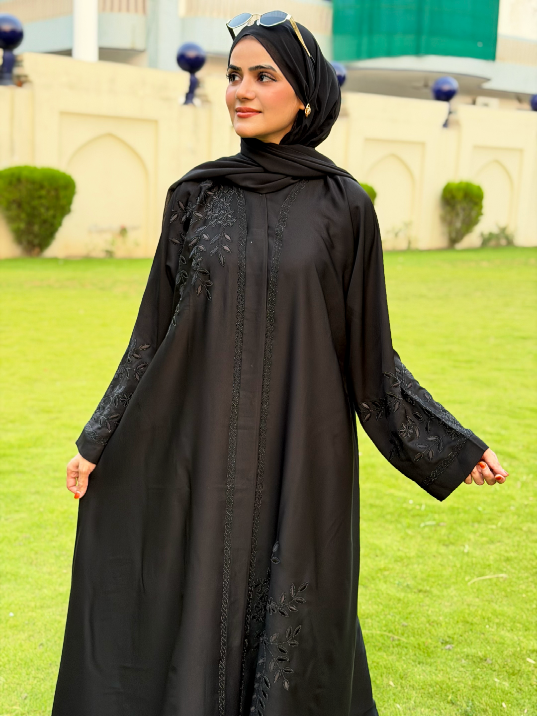 Woman wearing a black abaya with floral embroidery on a grassy field
