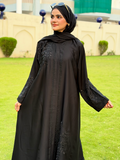 Woman wearing a black abaya with embroidery on a grassy field