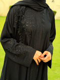 Black embroidered abaya on a person with a blurred green background