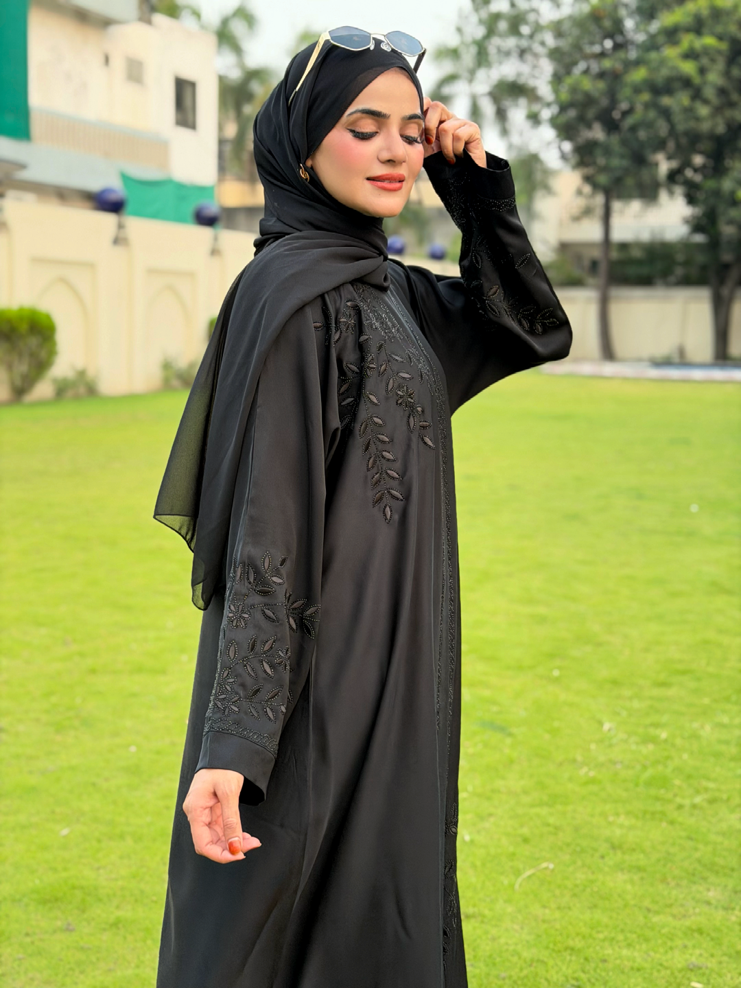 Woman in a black abaya with embroidery standing on grass