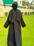 Person wearing a black abaya standing on grass with a building in the background